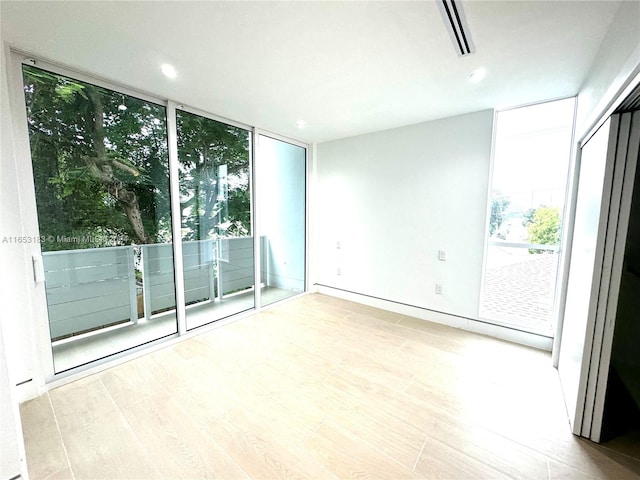 empty room featuring a wall of windows and light hardwood / wood-style flooring