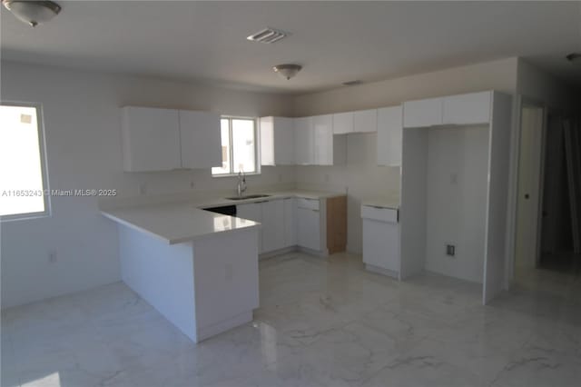 kitchen with a peninsula, a sink, visible vents, white cabinets, and marble finish floor