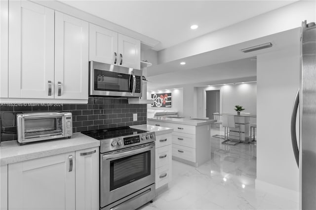 kitchen featuring kitchen peninsula, backsplash, appliances with stainless steel finishes, and white cabinetry