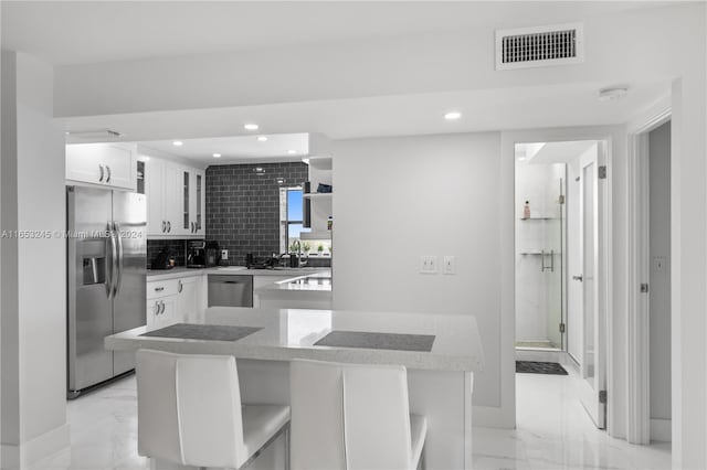 kitchen featuring a breakfast bar area, appliances with stainless steel finishes, white cabinetry, and tasteful backsplash