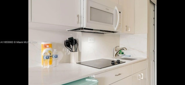 kitchen with black electric stovetop, sink, white cabinets, and decorative backsplash