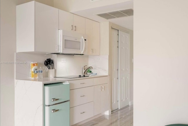 kitchen with stainless steel refrigerator, white cabinetry, backsplash, black electric cooktop, and light hardwood / wood-style floors