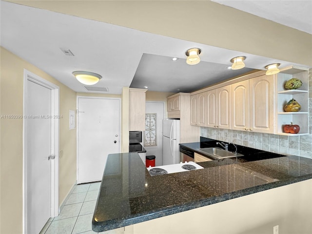 kitchen featuring dark stone counters, tasteful backsplash, kitchen peninsula, sink, and white refrigerator