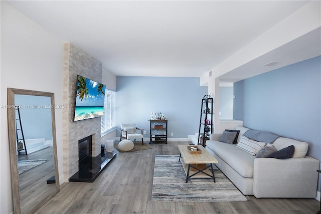 living area featuring baseboards, a fireplace, visible vents, and wood finished floors