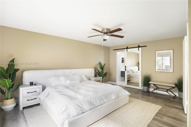 bedroom featuring baseboards, a barn door, a ceiling fan, and light wood-style floors