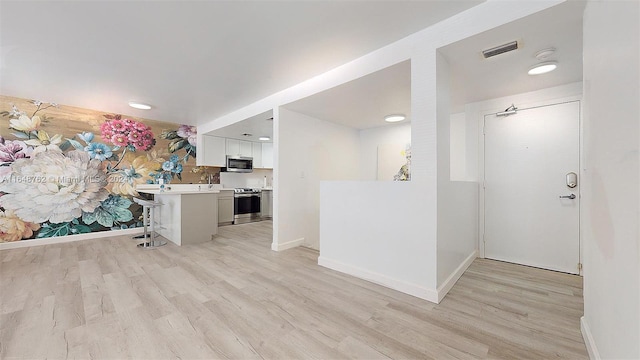 kitchen with a breakfast bar area, appliances with stainless steel finishes, white cabinetry, and light hardwood / wood-style floors