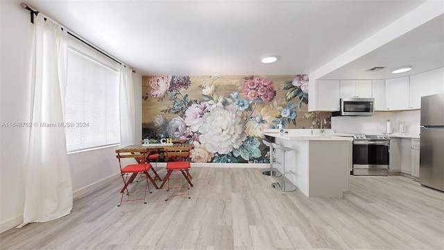 kitchen with a breakfast bar area, kitchen peninsula, stainless steel appliances, light wood-type flooring, and white cabinets