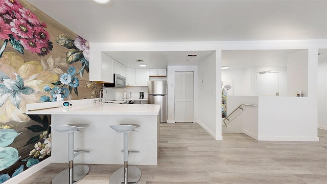 kitchen featuring kitchen peninsula, appliances with stainless steel finishes, a kitchen breakfast bar, white cabinetry, and light hardwood / wood-style flooring