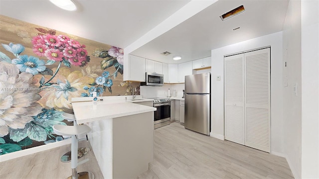 kitchen featuring kitchen peninsula, white cabinets, appliances with stainless steel finishes, a kitchen breakfast bar, and light hardwood / wood-style floors