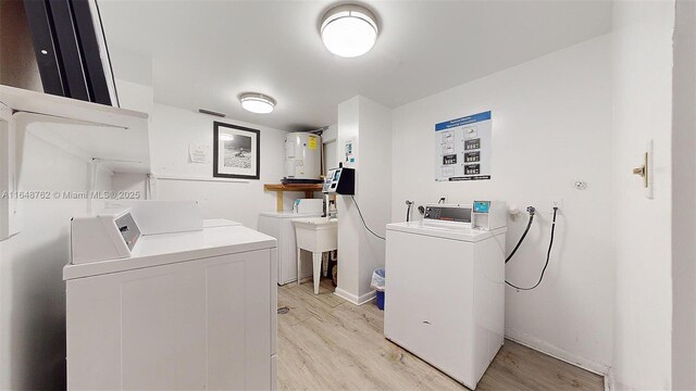 clothes washing area with electric water heater, washer and clothes dryer, and light hardwood / wood-style flooring