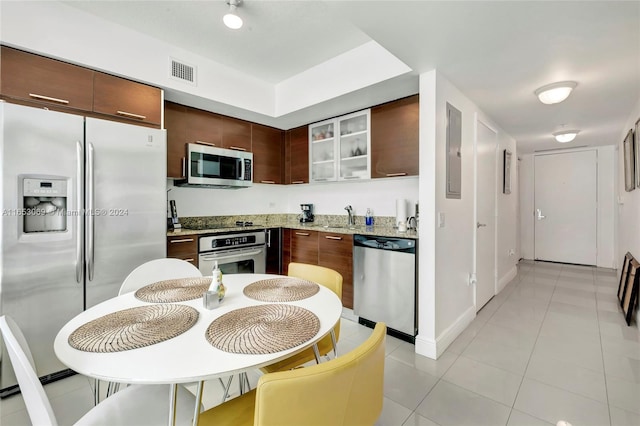 kitchen featuring light tile patterned floors, light stone countertops, stainless steel appliances, sink, and dark brown cabinets