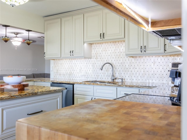 kitchen with white cabinetry, decorative light fixtures, light stone counters, sink, and stainless steel dishwasher