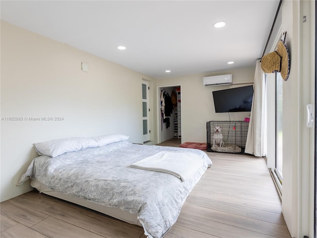 bedroom featuring light wood-type flooring, a walk in closet, a wall mounted air conditioner, and a closet