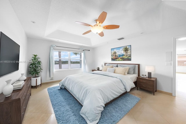 tiled bedroom with ceiling fan, a textured ceiling, and a tray ceiling