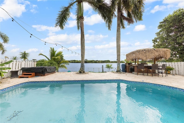 view of pool featuring an outdoor bar, a water view, and a patio area