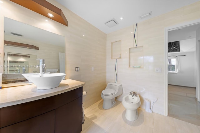 bathroom with a bidet, vanity, tile walls, tile patterned floors, and toilet