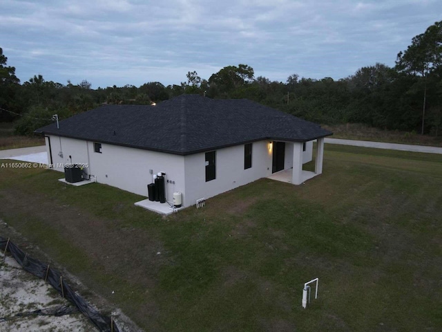 exterior space with cooling unit, roof with shingles, a yard, and stucco siding