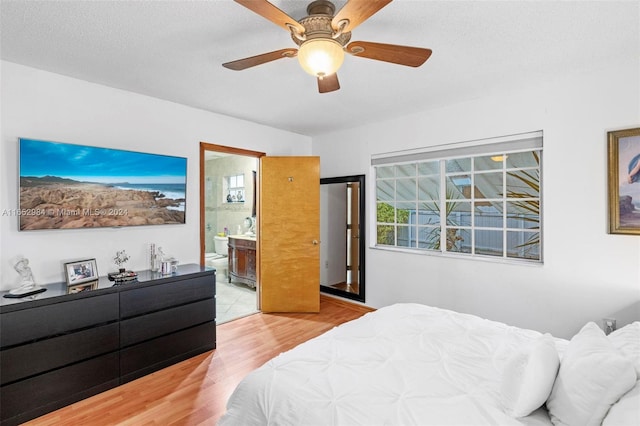 bedroom with ensuite bath, light wood-type flooring, a textured ceiling, and ceiling fan