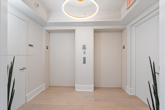 laundry area with a raised ceiling, light hardwood / wood-style floors, and elevator