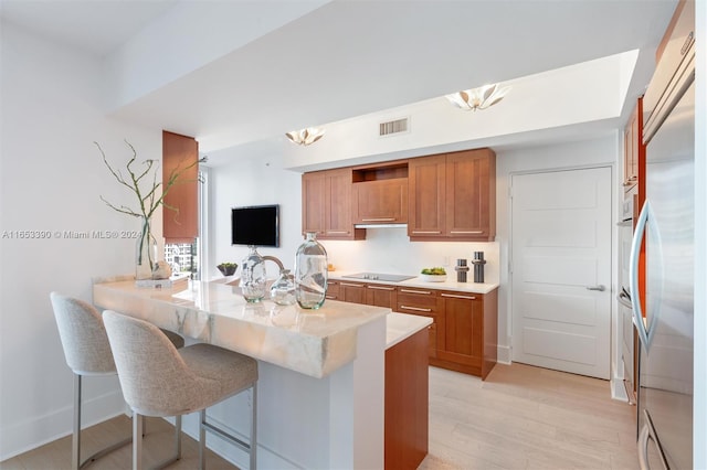 kitchen featuring kitchen peninsula, a breakfast bar, light hardwood / wood-style flooring, built in fridge, and black electric stovetop