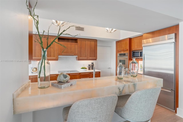 kitchen with appliances with stainless steel finishes, light wood-type flooring, a kitchen breakfast bar, and a notable chandelier