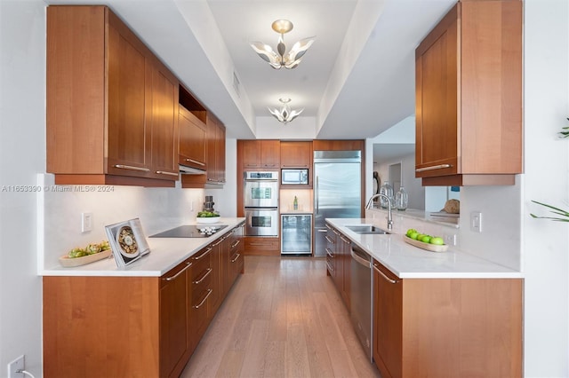 kitchen featuring built in appliances, beverage cooler, light hardwood / wood-style flooring, sink, and a notable chandelier