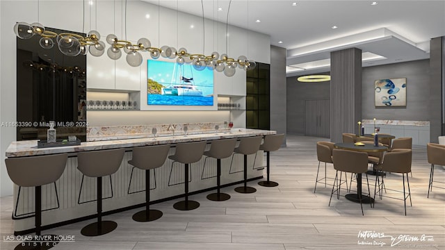 kitchen with white cabinetry, light stone counters, a breakfast bar, light hardwood / wood-style flooring, and decorative light fixtures