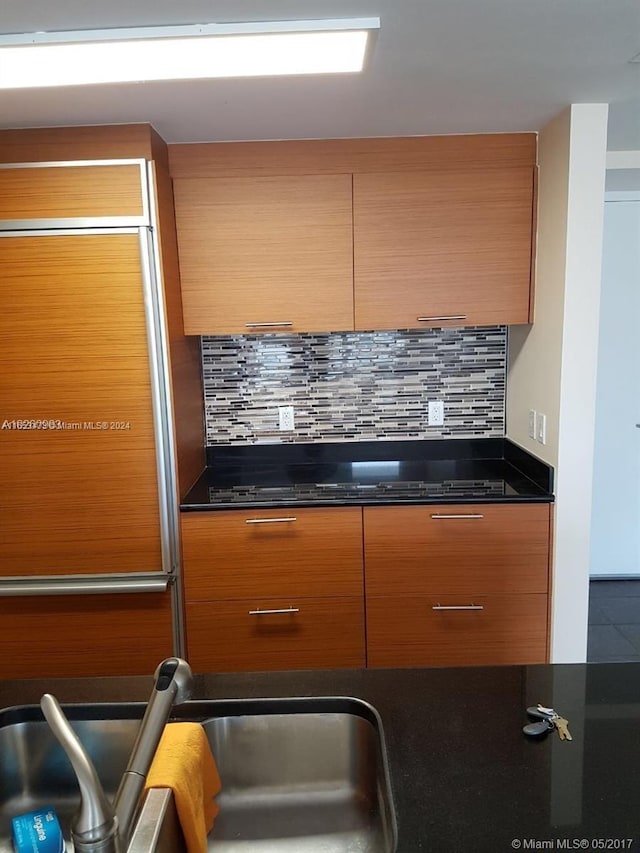 kitchen with decorative backsplash, dark stone counters, and sink