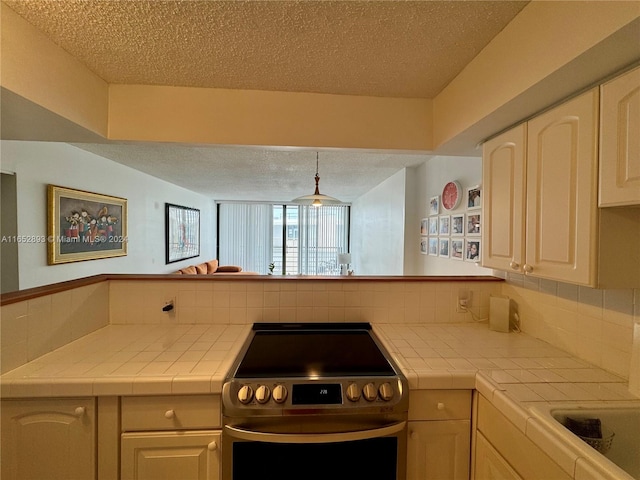 kitchen with tile counters, kitchen peninsula, stainless steel range with electric stovetop, and tasteful backsplash