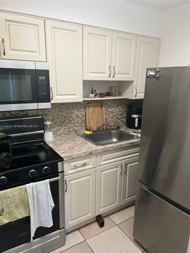 kitchen featuring backsplash, light tile patterned floors, appliances with stainless steel finishes, white cabinetry, and sink