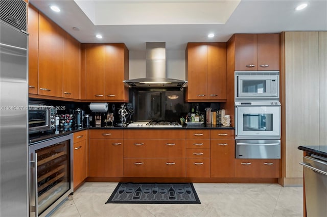 kitchen featuring wall chimney range hood, dark stone countertops, built in appliances, tasteful backsplash, and beverage cooler