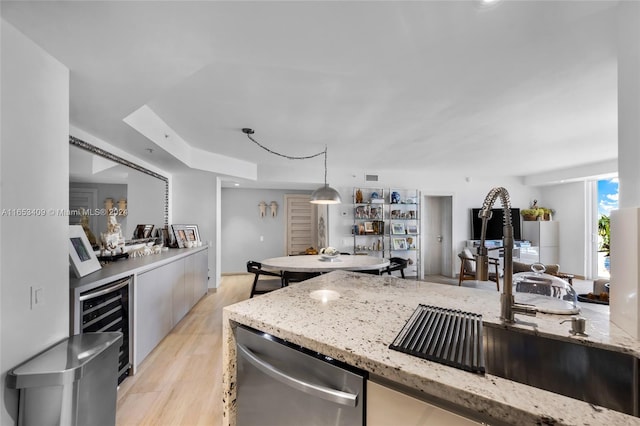 kitchen featuring beverage cooler, light stone counters, decorative light fixtures, and light hardwood / wood-style floors