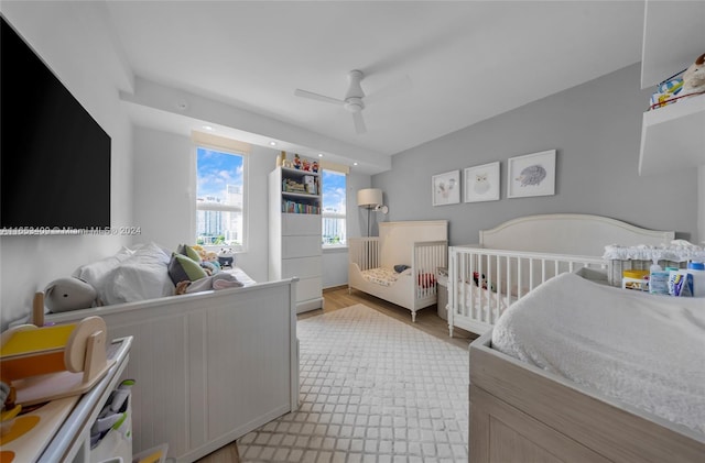 bedroom featuring a nursery area, ceiling fan, and light hardwood / wood-style floors