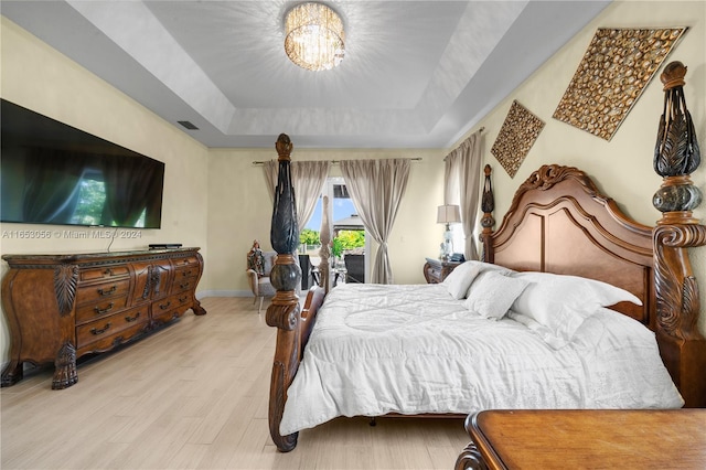 bedroom with a tray ceiling, a chandelier, and light hardwood / wood-style flooring