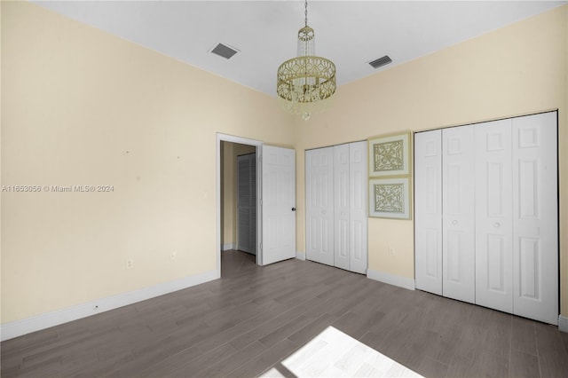 unfurnished bedroom featuring wood-type flooring, an inviting chandelier, and two closets