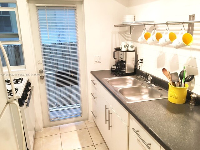 kitchen featuring white gas range, white cabinets, tasteful backsplash, sink, and light tile patterned flooring