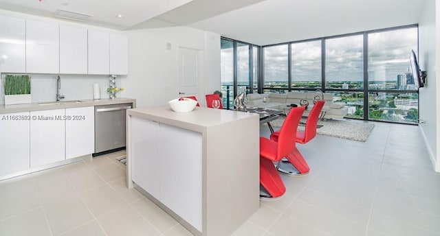 kitchen with a kitchen island, floor to ceiling windows, stainless steel dishwasher, sink, and white cabinetry