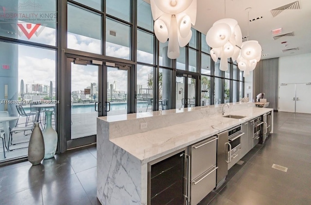 kitchen with sink, decorative light fixtures, a wall of windows, and light stone countertops