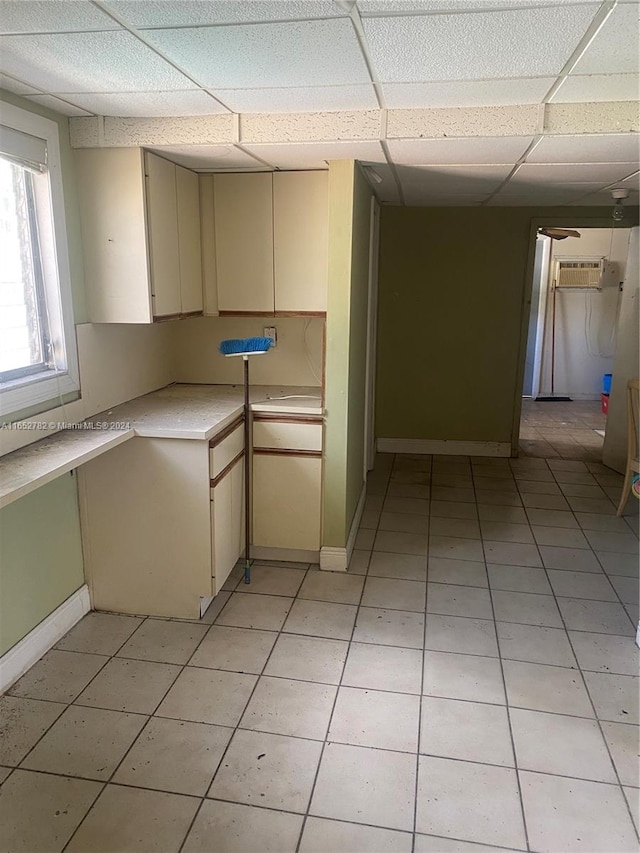 kitchen with a wall mounted air conditioner, light tile patterned floors, cream cabinets, and a drop ceiling