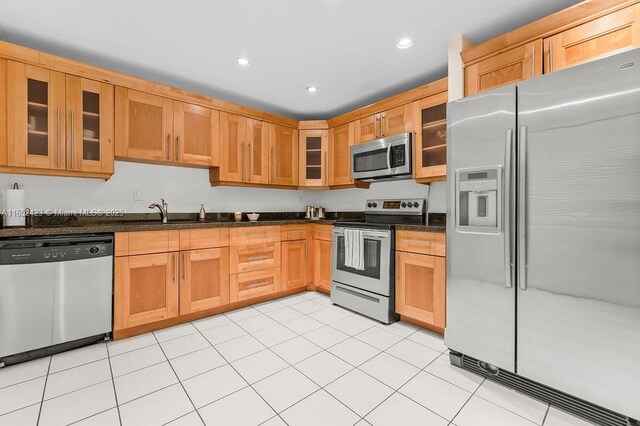 kitchen with sink, light tile patterned floors, stainless steel appliances, and dark stone counters