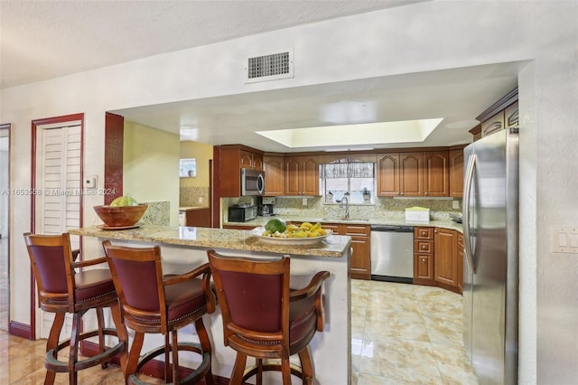 kitchen featuring light stone counters, tasteful backsplash, sink, kitchen peninsula, and stainless steel appliances