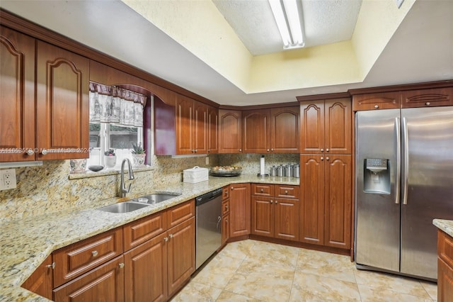 kitchen with sink, backsplash, appliances with stainless steel finishes, a tray ceiling, and light stone countertops