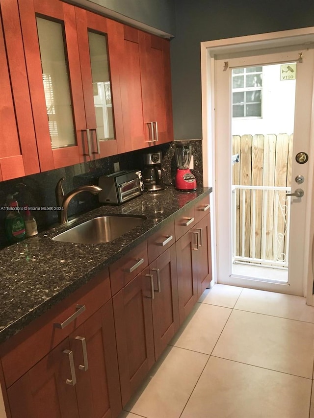 kitchen featuring dark stone counters, a wealth of natural light, light tile patterned floors, and sink