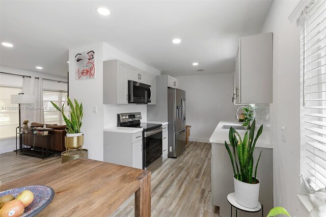 kitchen with stainless steel appliances, sink, light wood-type flooring, and white cabinets