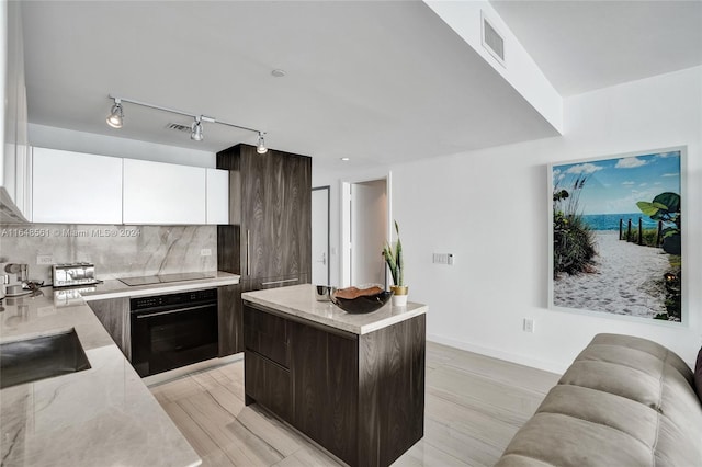 kitchen with a kitchen island, black appliances, rail lighting, light stone counters, and white cabinets