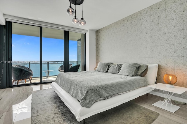 bedroom featuring a water view, a wall of windows, hardwood / wood-style floors, and access to exterior