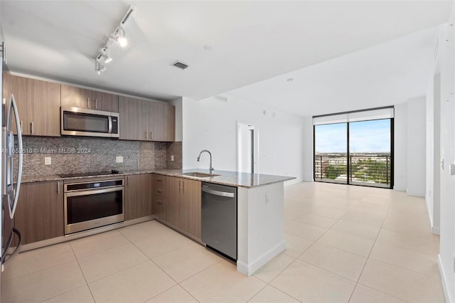 kitchen with dark stone countertops, appliances with stainless steel finishes, kitchen peninsula, and sink