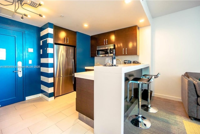 kitchen featuring a kitchen breakfast bar, dark brown cabinetry, kitchen peninsula, and stainless steel appliances