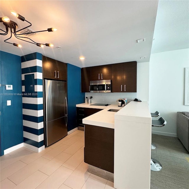 kitchen with kitchen peninsula, appliances with stainless steel finishes, decorative backsplash, a breakfast bar, and sink