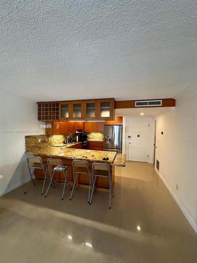 kitchen featuring a kitchen breakfast bar, kitchen peninsula, sink, stainless steel fridge with ice dispenser, and stone countertops